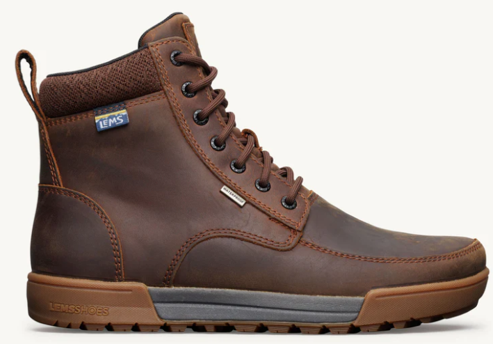 Load image into Gallery viewer, A brown leather high-top lace-up boot with a pull tab, black metal eyelets, and a brown and gray sole, shown from a side profile on a light off-white background. A small blue and white LEMS logo is visible on the ankle collar.