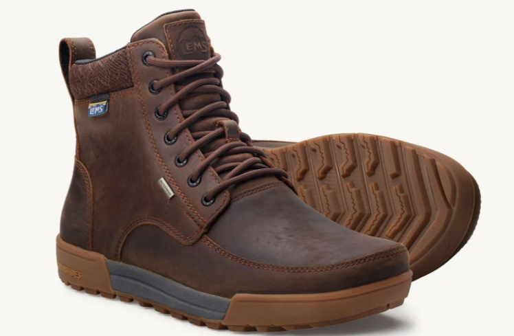 Load image into Gallery viewer, A pair of brown leather high-top boots with laces, shown on a clean off-white background. One boot is upright, showing the side and front, while the other lies on its side to display the treaded outsole.

