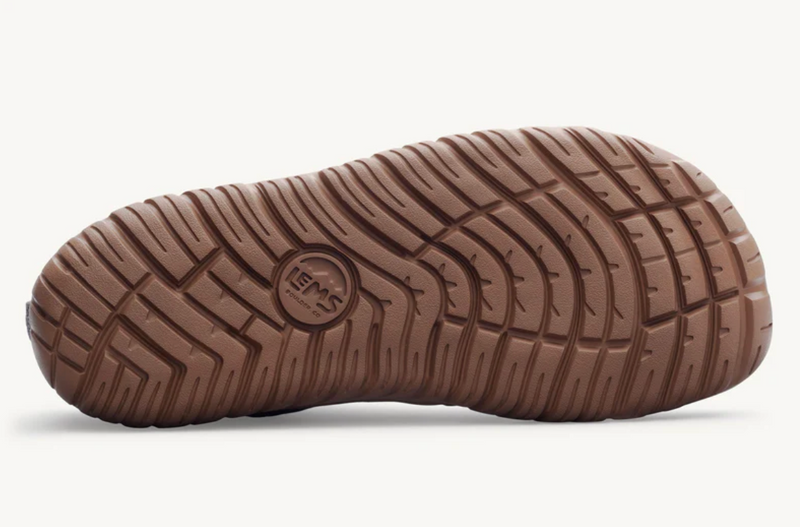 Load image into Gallery viewer, A close-up of a brown textured rubber shoe sole, showing the tread pattern and a circular Lems logo embossed in the center, set against a clean off-white background.

